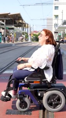 Modern tramvay raylarında motorlu sandalyede gezen kızıl saçlı kadın, şehir taşımacılık altyapısında kentsel hareketlilik ve kişisel bağımsızlığını gösteriyor.