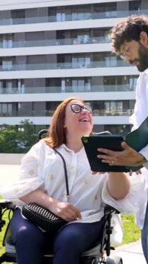 Profesyonel doktor, tekerlekli sandalyede oturan ve hasta merkezli sağlık hizmetleri etkileşimini vurgulayan gülümseyen engelli kadınla iletişim kurarken dijital tablet üzerinde tıbbi test sonuçlarını paylaşıyor.