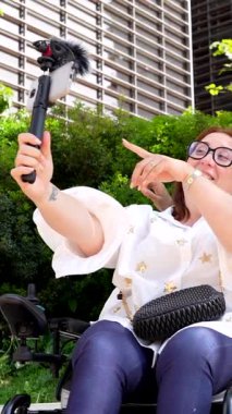 Tekerlekli sandalyede oturan memnun edici cep telefonu ve mikrofonla video kaydediyor, sonra da bir arkadaşıyla konuşuyor.