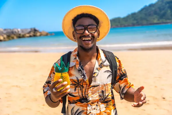 Genç adam, güneşli bir sahilde ferahlatıcı bir tropikal içecek tutarken gülümsüyor ve yaz tatili kaçamağının tadını çıkarıyor.