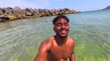 Işıl ışıl mavi sularda eğlenen turistler, güneşli gökyüzünün altında tropik plaj tatili boyunca kaygısız anların tadını çıkarırken neşe içinde su sıçratırlar.