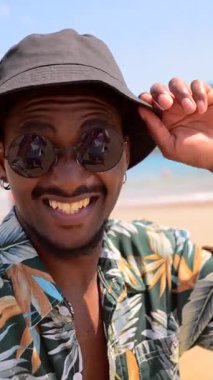 Turistler yaz tatilinden hoşlanıyor, güneşli bir sahilde selfie çekiyorlar, çeşitli yüz ifadeleri sergiliyorlar.