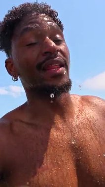 Genç Afrikalı Amerikalı adam yaz tatilinin tadını çıkarıyor, kristal berrak turkuaz suda yüzüyor, neşeli yüz ifadeleri ve kaygısız neşesiyle.