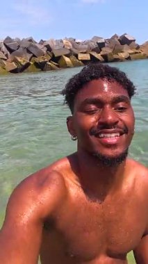 Yaz tatili boyunca ferahlatıcı deniz banyosu yapan genç bir adam güneşli mavi gökyüzü altında kaygısız anların ve boş vakitlerin tadını çıkarıyor.