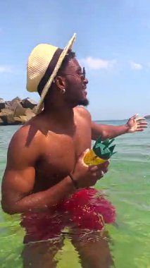 Genç adam güzel, berrak okyanus suyunda dinlenirken ferahlatıcı bir ananas kokteylinin tadını çıkarıyor.