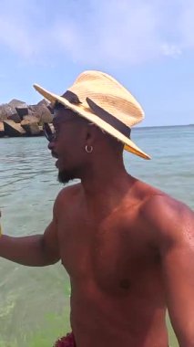 Tasasız genç siyah adam tropikal ananas kokteyli içerken berrak okyanus suyunda manzaralı arka planda dururken