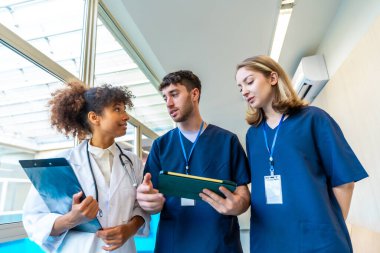 Doktorlar ve hemşireler tıbbi kayıtları ve röntgenleri inceliyor, hastane koridorunda hasta bakımında işbirliği yapıyorlar.