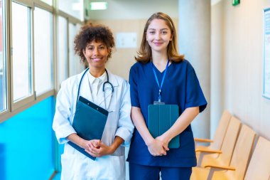 Hastane koridorunda tıbbi kayıtları tutarken gülümseyen doktor ve hemşire, sağlık sektöründe takım çalışması ve profesyonellik sergiliyor