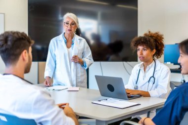 Modern bir hastane ortamında yapılan verimli bir toplantıda doktorlar ve tıp uzmanları işbirliği yapıyor, uzmanlıklarını paylaşıyor ve hasta bilgilerini analiz ediyorlar.