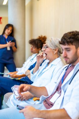 Yorgun doktorlar ve hemşireler hastane koridorunda oturup uzun bir vardiyadan sonra hastaları bekliyorlar.