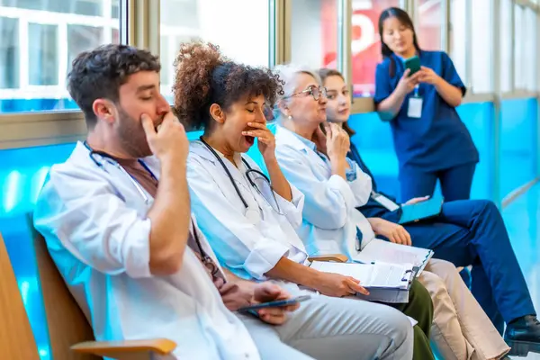 Hastane koridorunda sandalyelerde oturup uzun bir vardiyadan sonra yorgunluk çeken yorgun tıbbi uzmanlar esniyorlar.