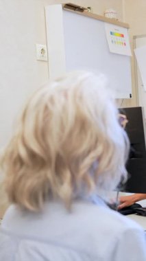 Tıbbi rehberlik sunan deneyimli kadın hekim, modern hastane ortamında dijital teknoloji kullanan kıdemli hastalarla sağlık detaylarını tartışıyor.