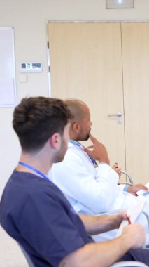 Doktorlar ve hemşireler bir hastane konferans odasında tıbbi bir sunuma katılıyor, dinliyor ve öğreniyorlar.