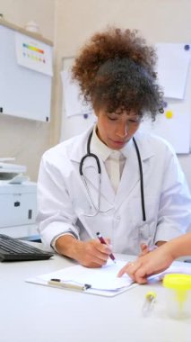 İki sağlık uzmanı bir ofis masasında hasta teşhisini tartışıyor, belgeleri inceliyor ve tıbbi kararlarda işbirliği yapıyorlar.