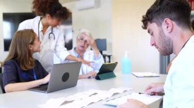 Doktorlar ve hemşireler birlikte çalışıp hasta bilgilerini bilgisayarda tartışıyorlar. Sağlık ortamında takım işbirliği ve karar verme