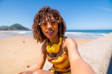 Yaz tatilinin tadını çıkaran bir turist. Okyanus dalgaları ve kumlu kıyılarla çevrili güneşlenirken neşeli bir selfie çekiyor.