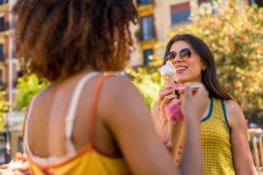İki arkadaş güneşli bir yaz gününde dondurma külahının tadını çıkarıyor, kahkahalarını paylaşıyor ve birlikte neşeli anılar yaratıyorlar.