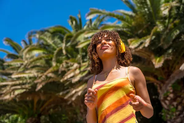 Canlı bir tropikal cennette kulaklık takan turist, güneşli mavi gökyüzünün altında sallanan palmiyelerle çevrili.