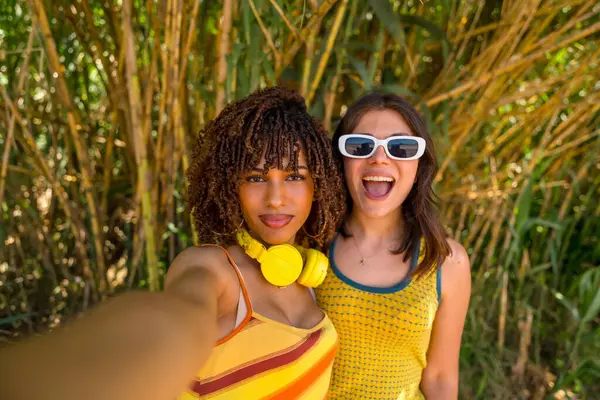 Canlı yeşilliklerle çevrili, yemyeşil bir bambu ormanında tatilin tadını çıkarırken neşeli bir selfie çeken iki kız arkadaş.
