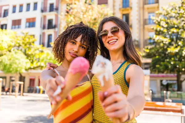 İki arkadaş şehirde güneşli bir günün tadını çıkarıyorlar. Sıcak güneş ışığında gülümserken renkli dondurma külahlarını kucaklayıp paylaşıyorlar.