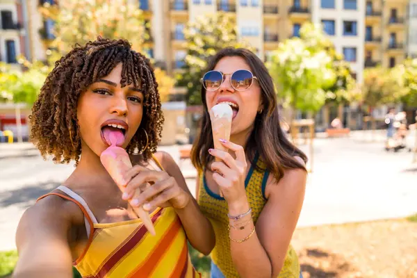 İki mutlu bayan arkadaş güneşli bir günde şehir parkında serinletici bir dondurma külahının keyfini çıkarıyorlar.