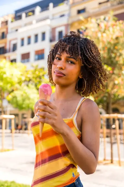 Şık genç bir kadın güneşli bir günde ferahlatıcı çilekli dondurma külahının tadını çıkarıyor.