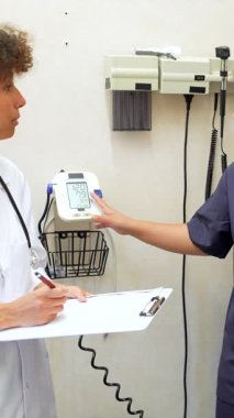 Tıp öğrencisi, klinik sağlık ortamında deneyimli doktorların rehberliği altında tansiyon ölçüm tekniği uyguluyor.