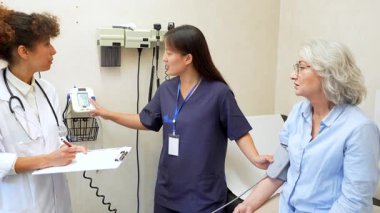 Hemşire ve doktor yaşlı hastaların kan basıncını ölçüyor, klinik ayarlarını tartışıyorlar.