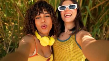 Kulaklık takan iki arkadaş selfie çekiyor, komik suratlar yapıyor ve doğayla iç içe vakit geçiriyorlar.