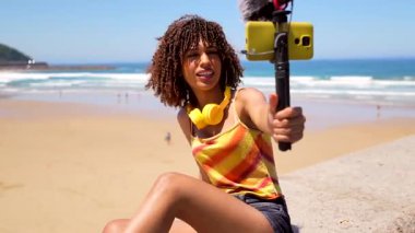İçerik yaratıcısı yaz yaşam tarzını yakalıyor, akıllı telefon ve dış mikrofon kullanarak kumlu sahilden video kaydediyor ve manzaralı okyanus arkaplanının tadını çıkarıyor.