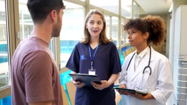 İş birliği yapan tıp uzmanları, hastane koridorunda yürürken hasta verilerini panolar ve dijital tabletler üzerinde inceleyerek profesyonel sağlık hizmetleri danışmanlığını gösteriyorlar.