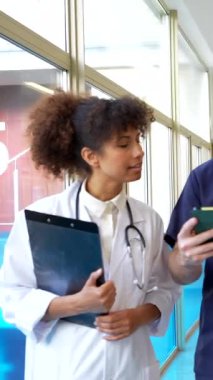 Doktorlar ve hemşireler hasta bilgilerini hastane koridorunda tablet ve pano kullanarak tartışıyorlar.