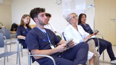 Konferans odasında oturan tıp uzmanları yoğun mesleki gelişim semineri sırasında dikkatle notlar dinliyor ve yazıyorlar.