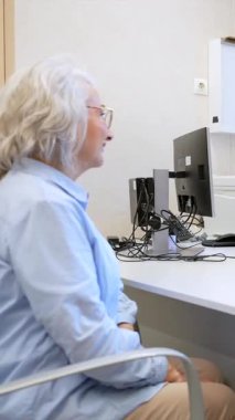 Yaşlı hasta doktorla sağlık sorunlarını tartışırken, hemşire de sağlık muayenehanesinde notlar alıyor.