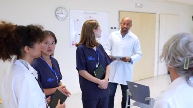 Doktorlar ve hemşireler bir hastane ortamında hasta bakımı stratejileri hakkında ortak bir tartışmaya katılıyorlar.