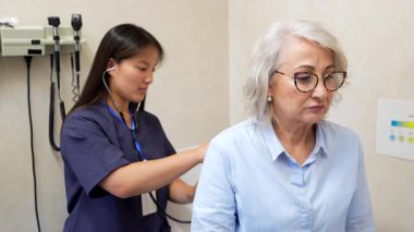 Tıbbi uzman, klinik ortamlarda solunum değerlendirmesi için steteskop kullanarak, sağlık kontrolü sırasında yaşlı kadınların akciğerlerini dikkatlice inceliyor.