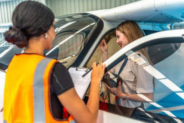 Uçak bakım şefi kontrol listesi tutuyor, kokpitte oturan bayan pilotla konuşuyor, kalkışa hazırlanıyor.