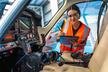 Kadın uçak bakım mühendisi uçuş öncesi kontrol sırasında kokpit panelini incelerken not alıyor.