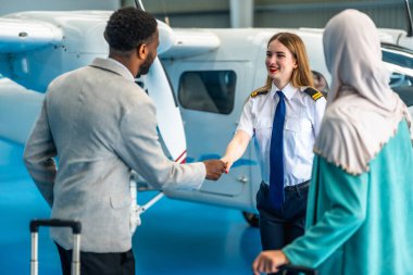 Kadın pilot, bir hangarın içinde iş adamıyla el sıkışıyor. Yanında bir iş kadını bekliyor.