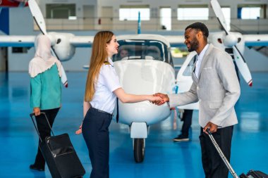 Kadın pilot bir uçak hangarında iş adamıyla el sıkışıyor, özel bir uçuştan önce bir yolcuyu selamlıyor.