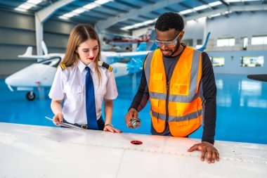 Uçak bakım mühendisi, bir hangarda uçuş öncesi kontrol sırasında pilota yakıt örneği gösteriyor.