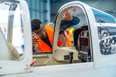 Güvenlik gözlüğü takan ve görüş mesafesi yüksek bir yelek giyen uçak mühendisi uçak hangarındaki küçük bir uçağın kokpitini inceliyor.