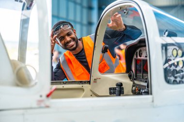 Gülümseyen uçak bakım mühendisi hangardaki uçuş öncesi kontroller sırasında küçük bir uçağın kokpitinden el sallıyor.