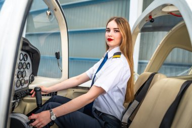 Kendine güvenen bayan pilot küçük bir uçağın kokpitinde oturuyor, kontrol çubuğunu tutuyor ve kalkışa hazırlanıyor.