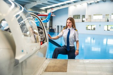 Kendine güvenen bayan pilot hangarda küçük bir uçağa biniyor, heyecan verici bir uçuşa hazırlanıyor ve önlerindeki macerayı kucaklıyor.