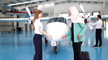 Profesyonel kadın pilot, uçak hangarında özel bir jete binmeden önce yolcularla el sıkışıyor.