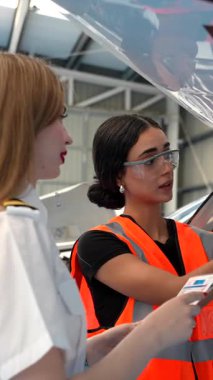 Turuncu yelek giyen ve güvenlik gözlüğü takan tamirci, amirinden uçak parçalarını tamir etmesi için talimat alıyor.