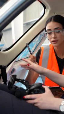 Genç bayan pilot uçuş öncesi eğitim sırasında kompakt uçak kokpitindeki kulaklığı ayarlarken eğitmenden rehberlik alıyor.