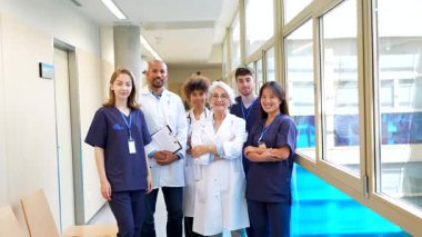 Profesyonel tıbbi ekip bir arada duruyor. Parlak hastane koridorunda poz verirken özgüvenle gülümsüyor. İş yeri ekip çalışması ve uzmanlığını sergiliyor.