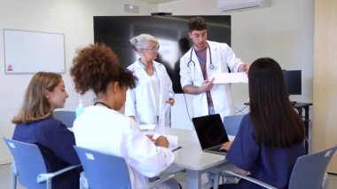 Doktorlar ve hemşireler hastane konferans odasında teşhis ve tedavi planlarını tartışarak tıbbi kayıtları gözden geçirirler.